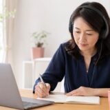 英語音声を聞きながらノートに書き取るディクテーション練習中の社会人女性